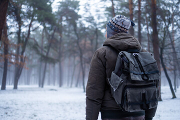 Hiking man with backpack walking in winter foggy forest covered snow. Adventure people in wild nature.