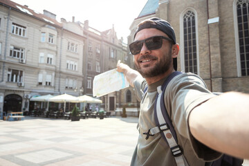 Man tourist wearing sunglasses taking selfie while exploring sights of city.