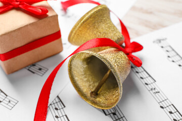 Golden shiny bells with red bow, gift box and music sheets on table, closeup. Christmas decoration
