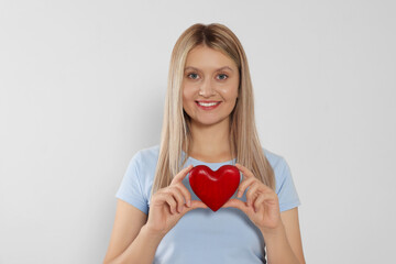 Happy volunteer holding red heart with hands on light background