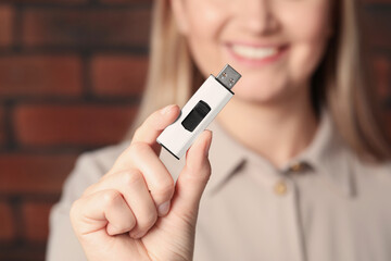 Woman holding usb flash drive near brick wall, focus on hand