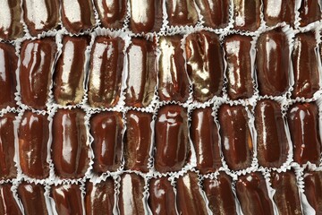 Many delicious eclairs with chocolate icing as background, top view