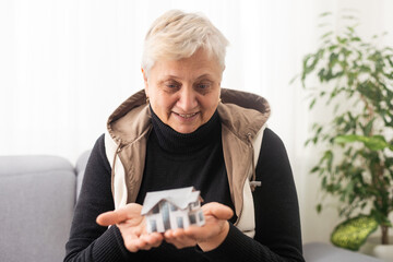 Happy realtor woman holding tiny house model on hand, palm, showing object at camera, promoting...