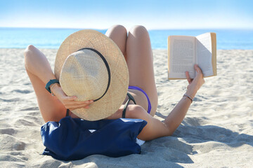 Fototapeta na wymiar Woman reading book on sandy beach near sea