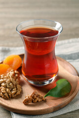 Board with glass of traditional Turkish tea, walnuts and dried apricots on wooden table, closeup