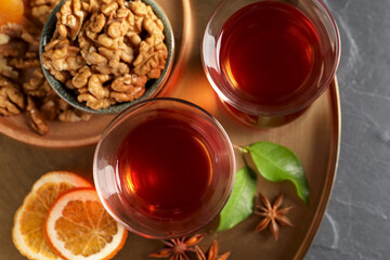 Tray with glasses of traditional Turkish tea, walnuts, dried orange and anise on black table, top view