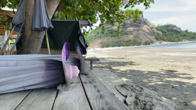 Beachfront view folded purple umbrella, tree and mountain near sandy beach on sunny day. Hua Hin beach