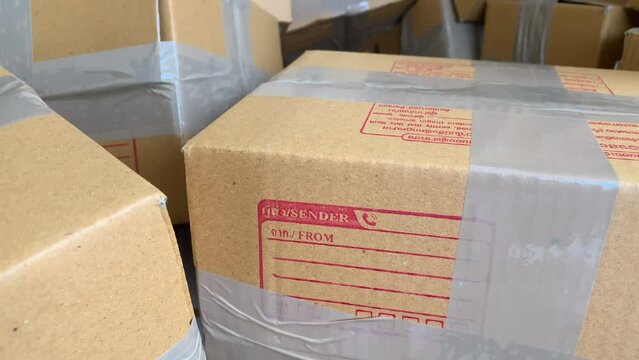 Close up cardboard box package with sender and postcode word screen on parcel with pile of wrapped boxes 