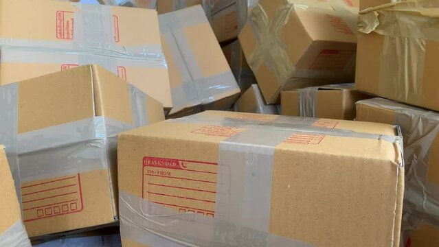 Close up cardboard box package with sender and postcode word screen on parcel with pile of wrapped boxes 