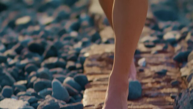 Young girl walking tiptoe with on the sea shore with sun reflection in the crushing waves. Rest and vacation on the beach by the sea.
Cheerful and joyful blonde walks barefoot on the rocks. 