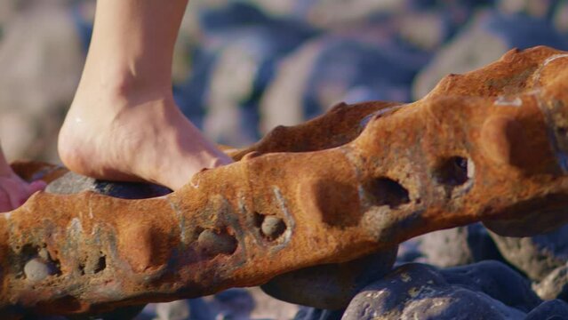 Legs close up. The girl steps on a rusty metal structure. Beautiful feet barefoot on a rocky beach. Move on the hard surface.