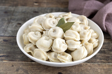Dumplings or russian pelmeni with meat and bay leaf in a white plate on a wooden background. Selective focus.