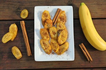 Tasty deep fried banana slices and cinnamon sticks on wooden table, flat lay - Powered by Adobe