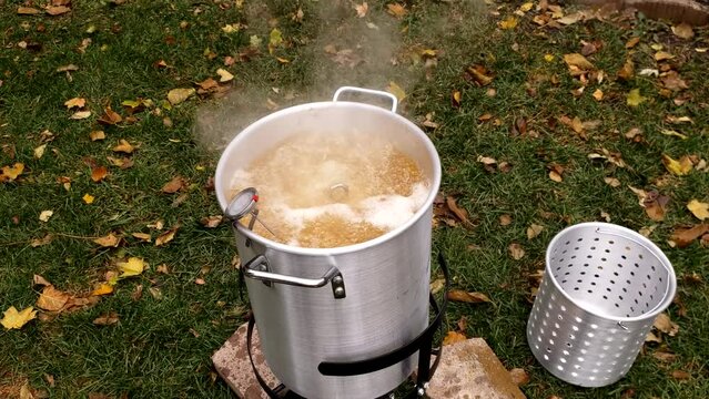 oil boils and steam rise while turkey being deep fired in large pot at back yard.