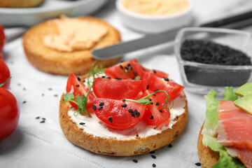 Fototapeta na wymiar Tasty rusk with cream cheese, fresh tomatoes and black sesame seeds on white table, closeup