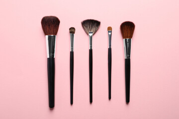 Different makeup brushes on pink background, flat lay