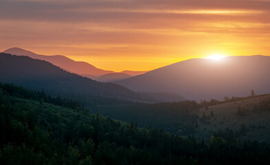 Amazing nature scenery. Atmospheric foggy mountain landscape during sunset. Beautiful vivid landscape in the mountains with colorful sky and silhouettes of mountains under sunlight. Creative image