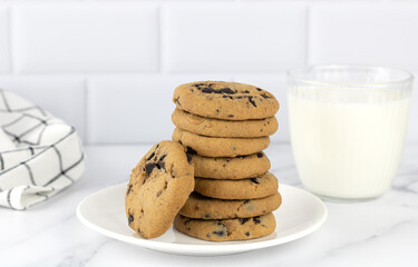 A bowl of freshly baked chocolate chip cookies and a glass of milk in a white kitchen. Copy space. National Cookie Day.