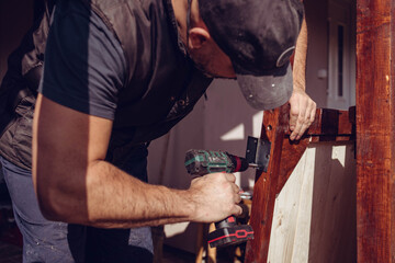 Handyman screwing a door hinge in the wooden door frame. Home renovation