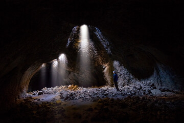 Adventurous athletic male standing in a lava tube looking at the sunlight shinning down into the...