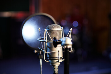 Fototapeta na wymiar Microphone with a pop shield closeup on the background of a professional recording studio. Microphone stand with a condenser for records vocals, speakers and sound of musical instrument. 