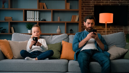 Bored child girl resting at home with father young dad using mobile phone little kid need attention...