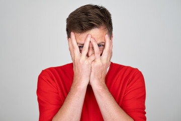 Scared man hides face behind palms, peeks through fingers, feels frightened 