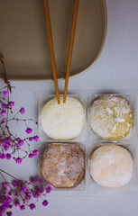 Traditional Japanese dessert mochi in rice dough or daifuku. Mochi ice cream balls and gray plate, food chopsticks on blue background flatly. Table setting detaails, violet flowers. Selective focus.