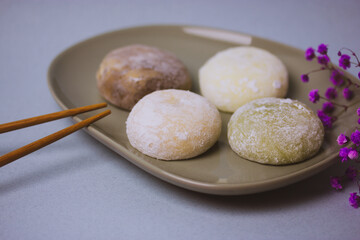 Traditional Japanese dessert mochi in rice dough or daifuku. Mochi ice cream balls and gray round plate, food chopsticks on blue background flatly. Table setting, violet flowers decor. Selective focus