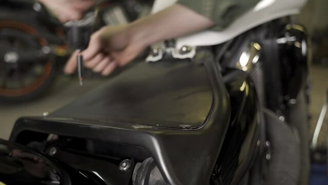 An auto mechanic unscrews the nuts securing a motorcycle part with a screwdriver. Close-up.
