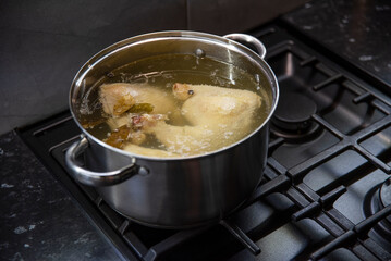 Gotujący się wywar drobiowy w dużym stalowym garnku na czarnej kuchence gazowej