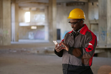 African american workman in yellow hard hat with smartphone