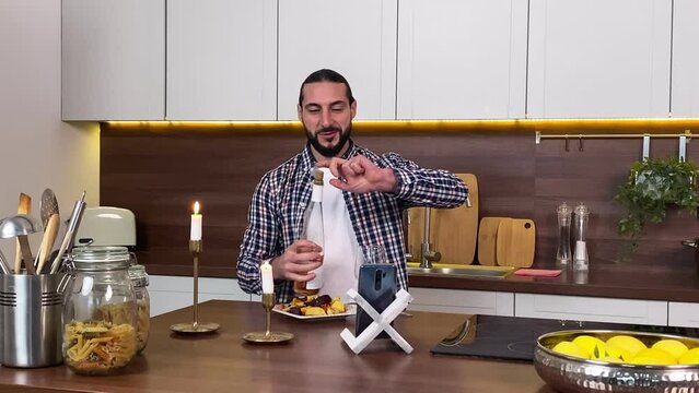 Handsome bearded adult man having date by using online dating service via Internet mobile app indoors. Charming boyfriend cheers partner with glass of wine while remote rendezvous at home. Romance