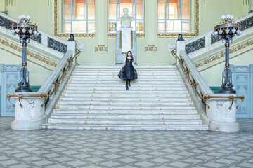 Beautiful girl in black dress running down wide stairs in hall checkered floor. High quality photo