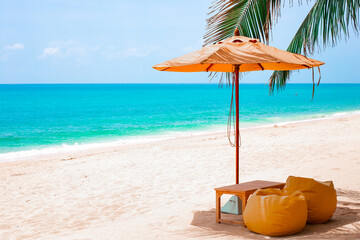 An ideal tropical beach with white sand, azure sea, with a parasol and soft poufs. Rest on vacation