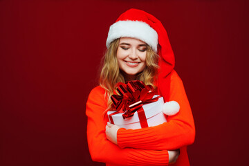 a beautiful young woman in a Santa Claus hat with a gift on a red background. 