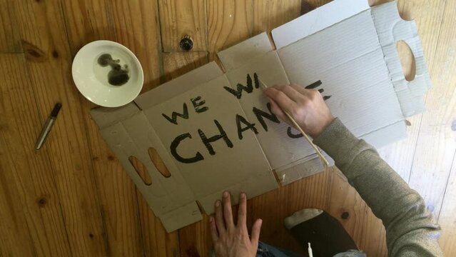 A environmental protestor writing and painting a sign that reads We want change