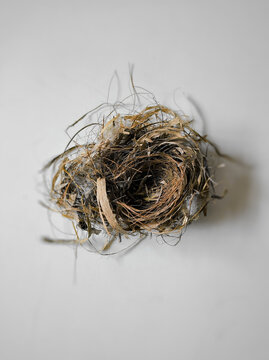 A lonely bird's nest made of grass and straw empty with no eggs and messy on the white and gray floor