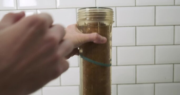 Man pulls out a dirty water pre-filter cartridge. Cartridge replacement concept. Transparent plastic flask.