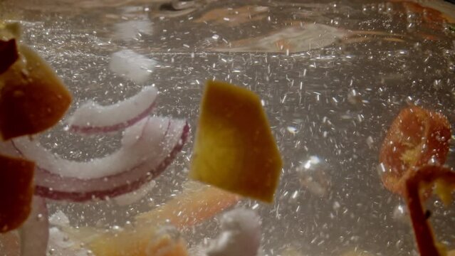 Slow motion background video of fresh organic vegetables in boiling water. Cooking onions carrots peppers in hot water in the kitchen. High quality 4k footage