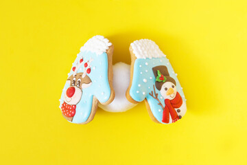 Two colorful Christmas biscuits in the shape of gloves holding a snowball against yellow background. Minimal surreal concept for winter season banner or print. Design for season greetings card.