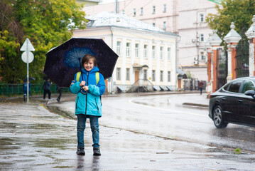 ortrait of a smiling schoolboy with an umbrella on a rainy day outside