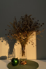 Bouquet of dried flowers on the table in a glass vase, in the light of the sun, contrasting image, with bright shadows