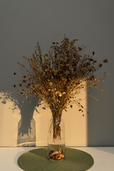 Bouquet of dried flowers on the table in a glass vase, in the light of the sun, contrasting image, with bright shadows