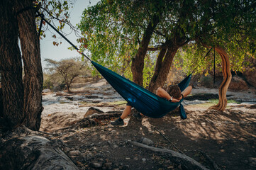 Frau chillt in einer blauen Hängematte unter einem Baum in der Mittagssonne, Warmquelle, Namibia