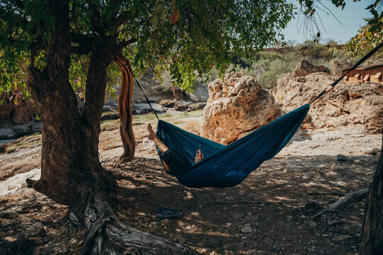 Frau chillt in einer blauen Hängematte unter einem Baum in der Mittagssonne, Warmquelle, Namibia