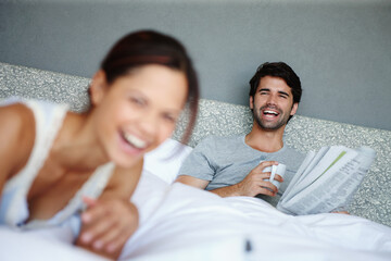 Relaxed and happy. Shot of a man in bed smiling at his girlfriend with a newspaper and mug in his hand.