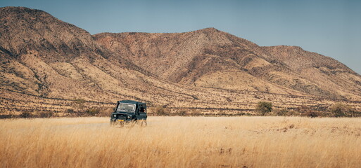 Panorama - Geländewagen steht vor bergigerer Kulisse im hohen Gras in der Ebene des Damaralandes, Namibia © Michael