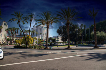 Obraz na płótnie Canvas a street lined with tall lush green palm trees in front of Union Station train station with cars and trucks driving on the street and storm clouds with lightning in Los Angeles