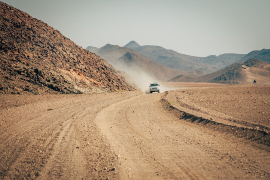 Ein weißes Auto fährt über eine staubige Gravel Road im Kakokoveld, Kunene, Namibia